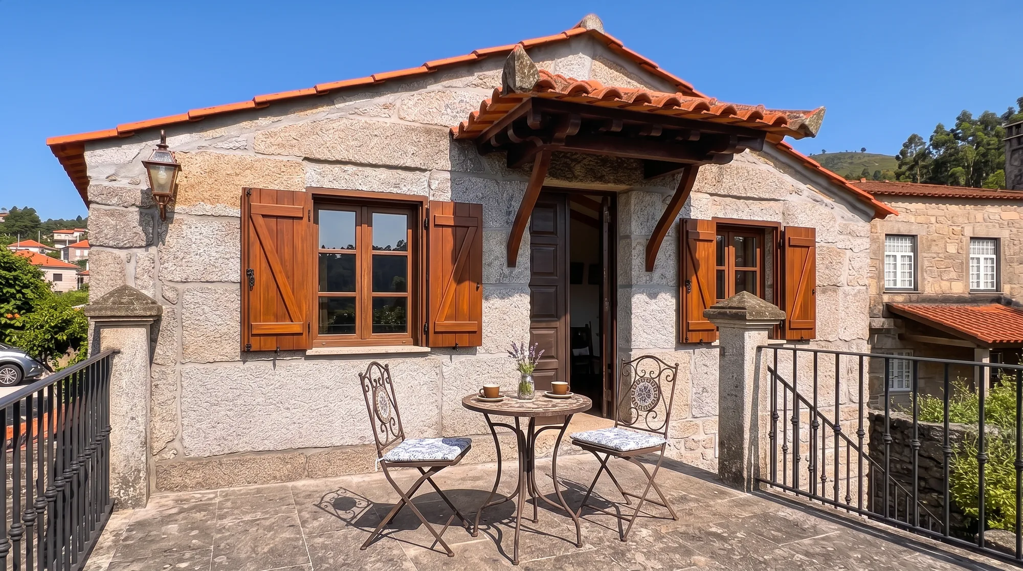 Stone guest house exterior with a terrace, bistro table and chairs, and wooden shutters