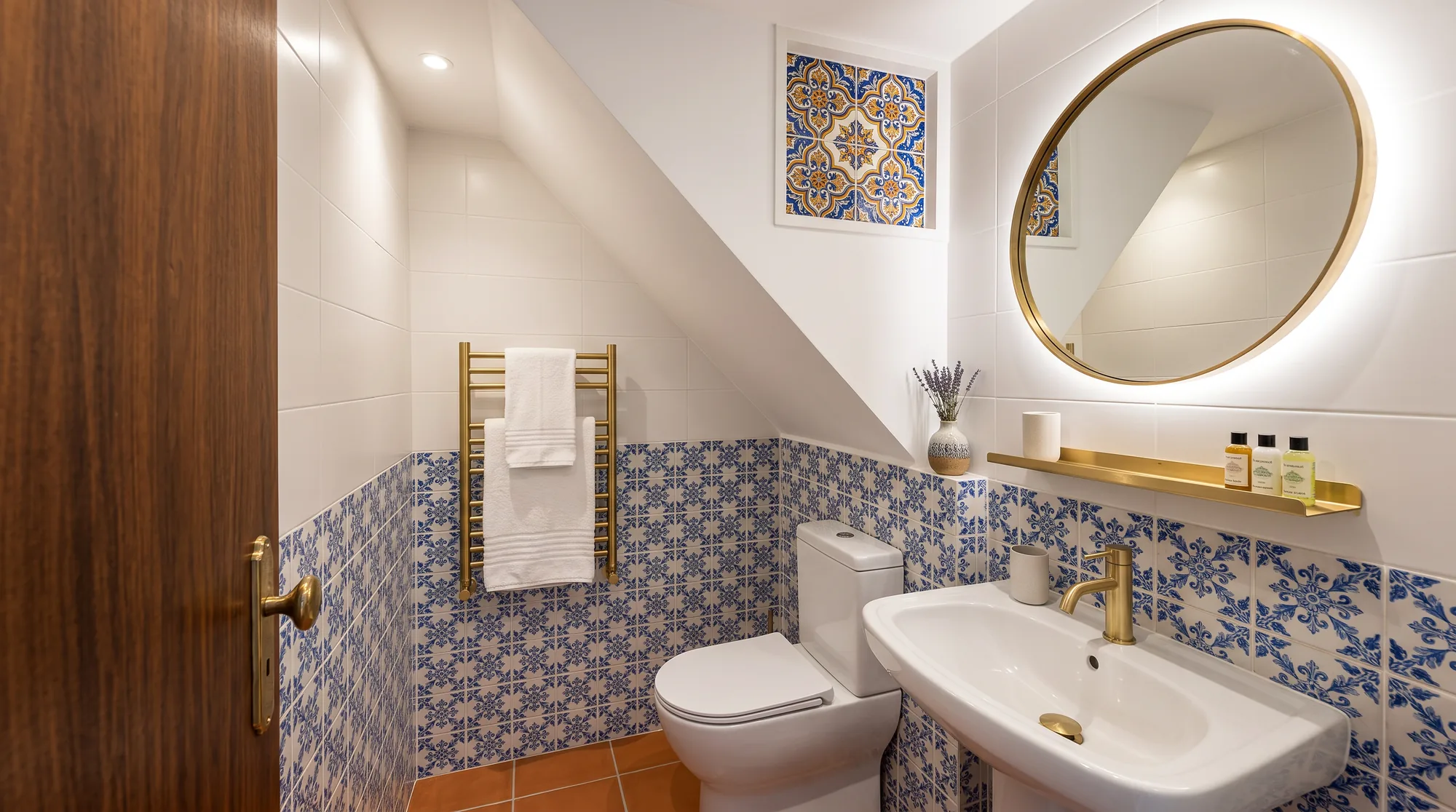 Guest house bathroom tiled in blue and white azulejo patterns, with a round brass mirror
