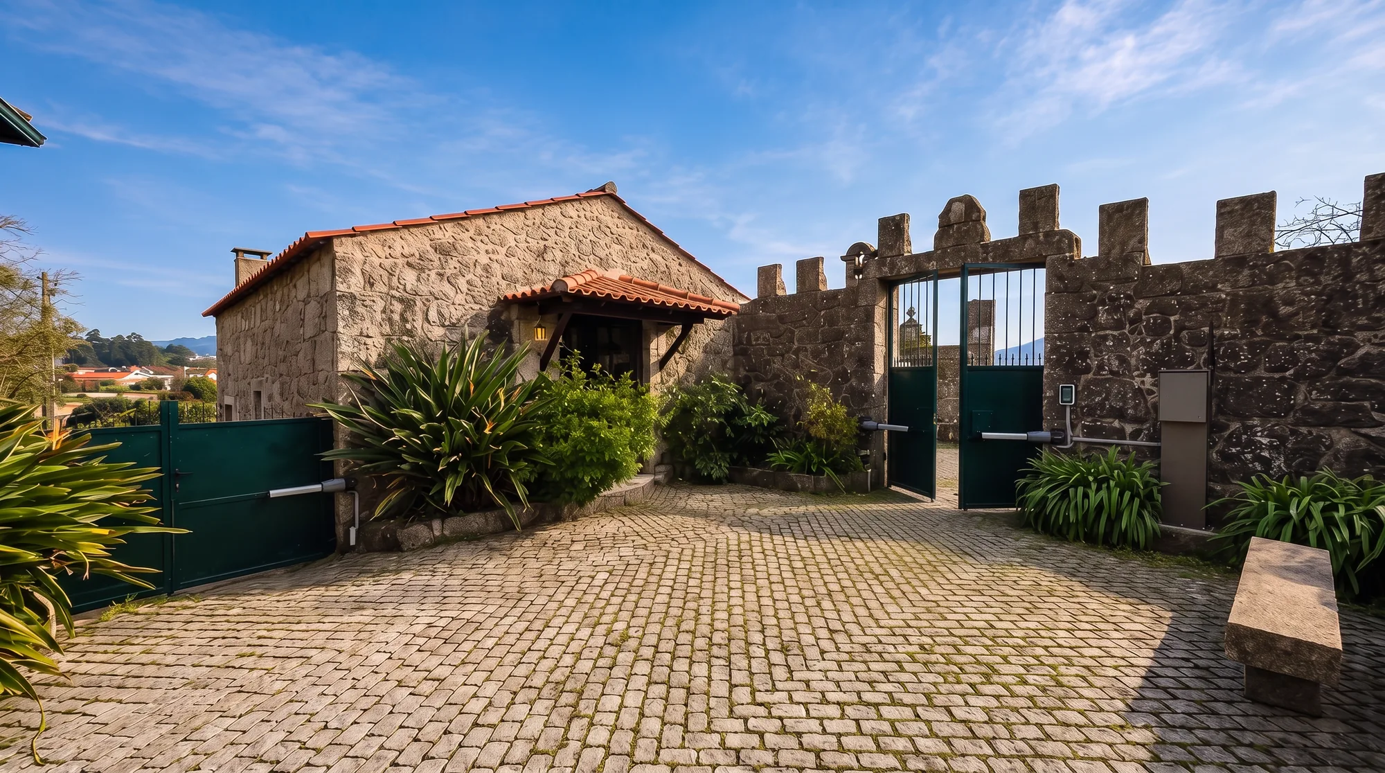Back gate with automatic opener, set into a castellated granite wall, with the stone guest house visible behind it