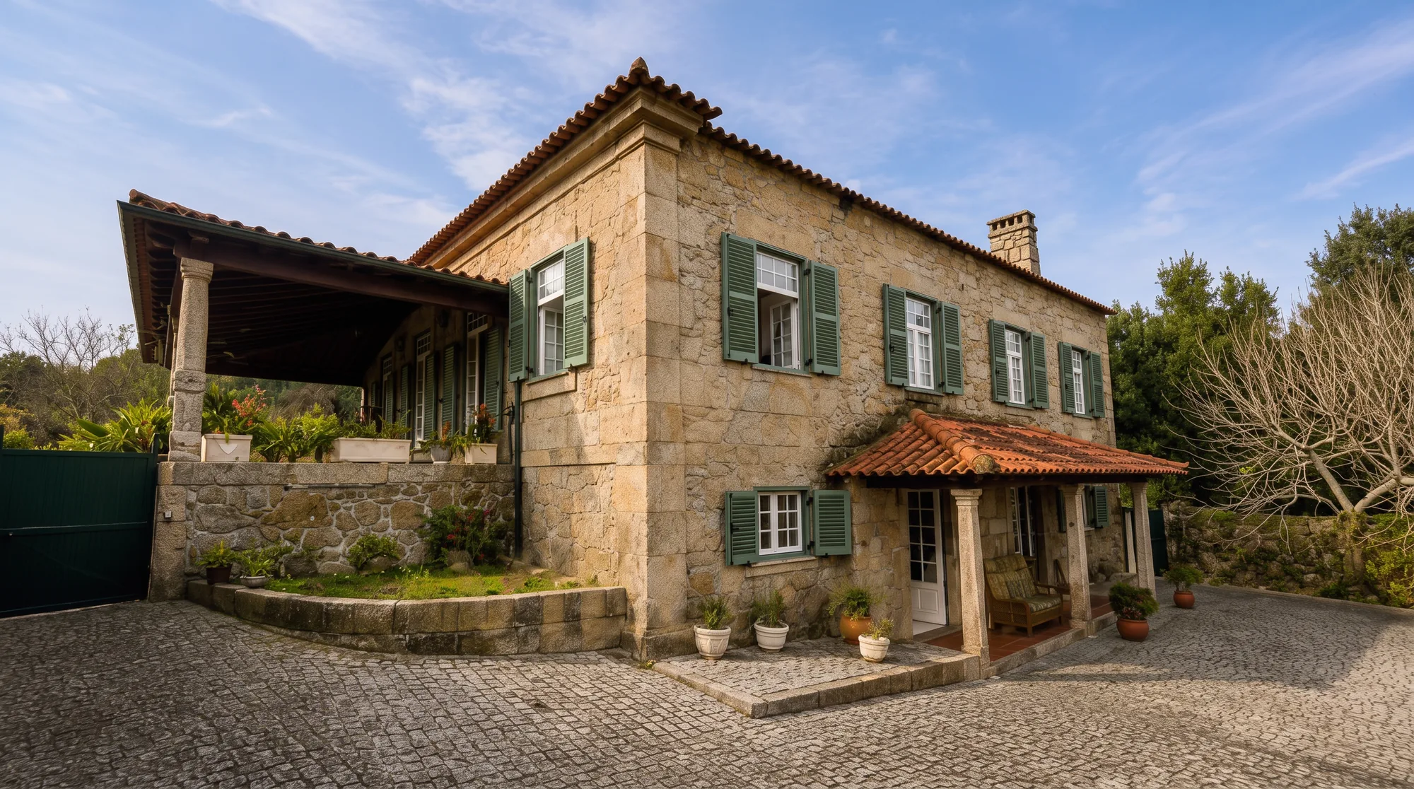 Corner view of the main house, two-storey granite with green shutters and a covered stone porch