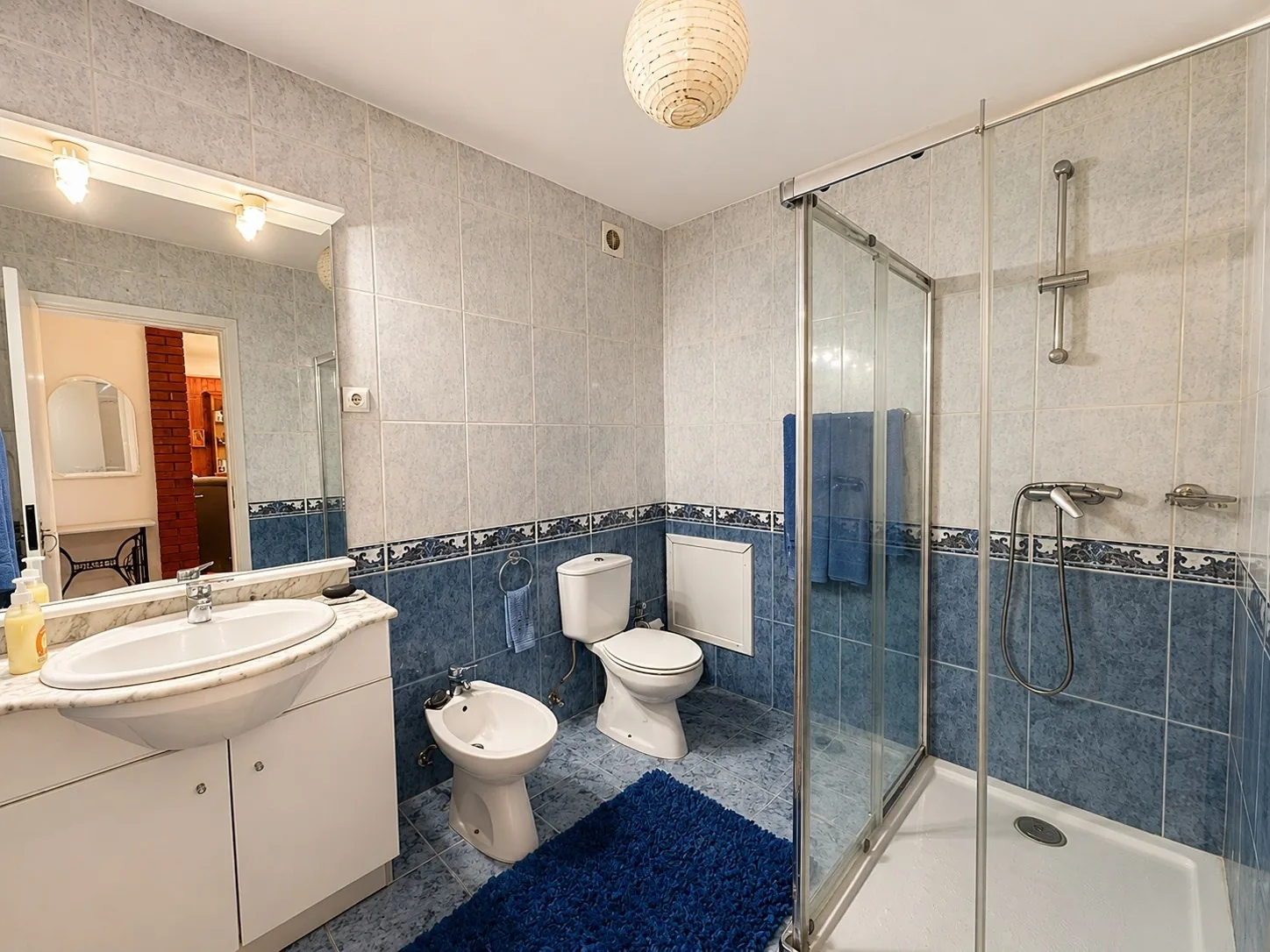 Second bathroom with blue tile, a glass shower enclosure, sink, toilet, and bidet