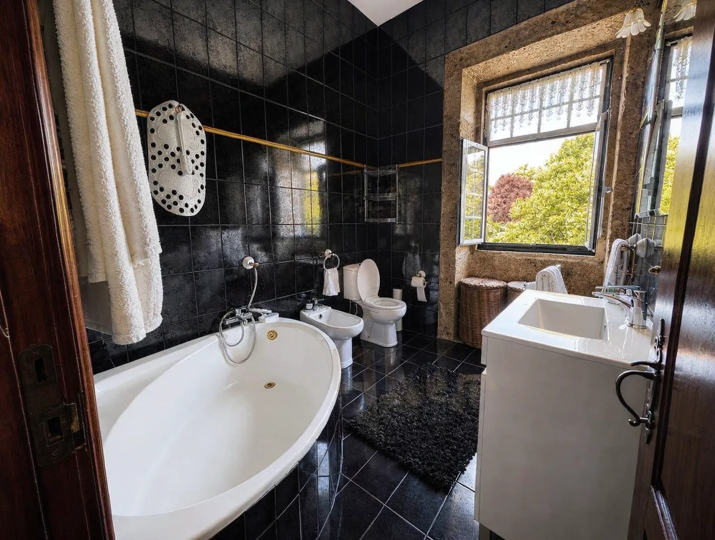 Bathroom with a deep soaking tub, bidet, and dark tile, with a window open to the garden