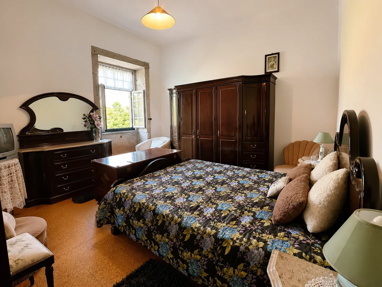 Bedroom with a large dark wardrobe, a dressing table with mirror, and a floral bedspread